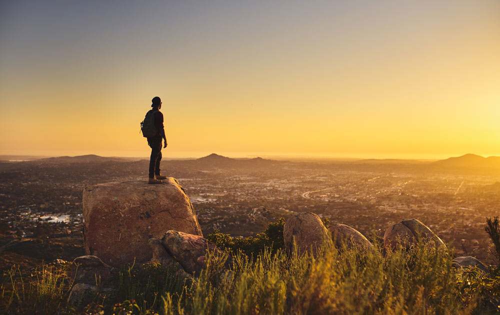 Mann schaut bei Sonnenuntergang von einem Berg auf San Diego