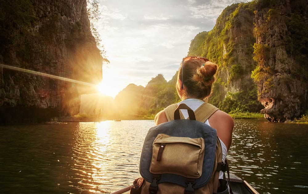 Frau mit Rucksack blickt bei Sonnenuntergang auf einen Fluss